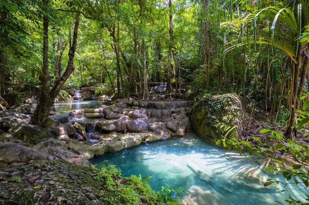 Explore the serene beauty of a lush Thai rainforest with stunning waterfalls cascading into tranquil pools. 泰国佛牌与法事内容说明图